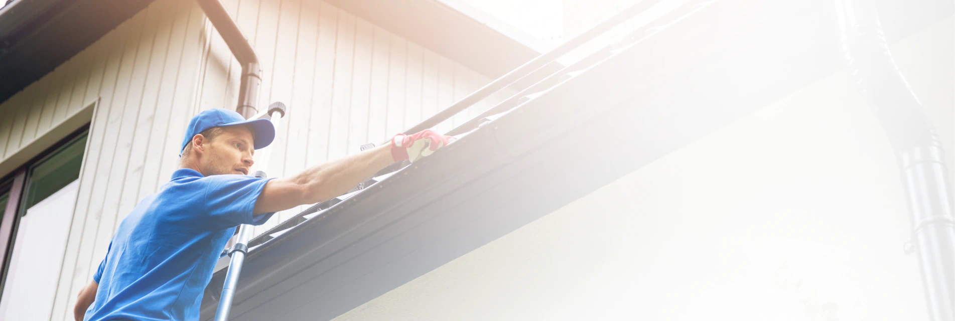 worker on ladder cleaning gutter